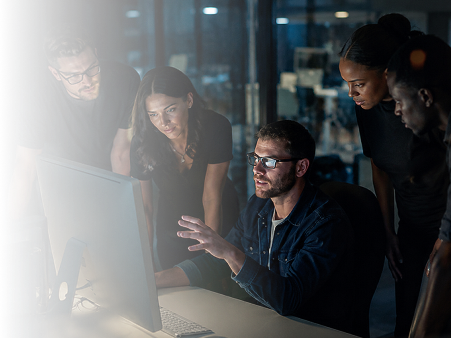 Security team collaborating around a monitor in a dimly lit office.